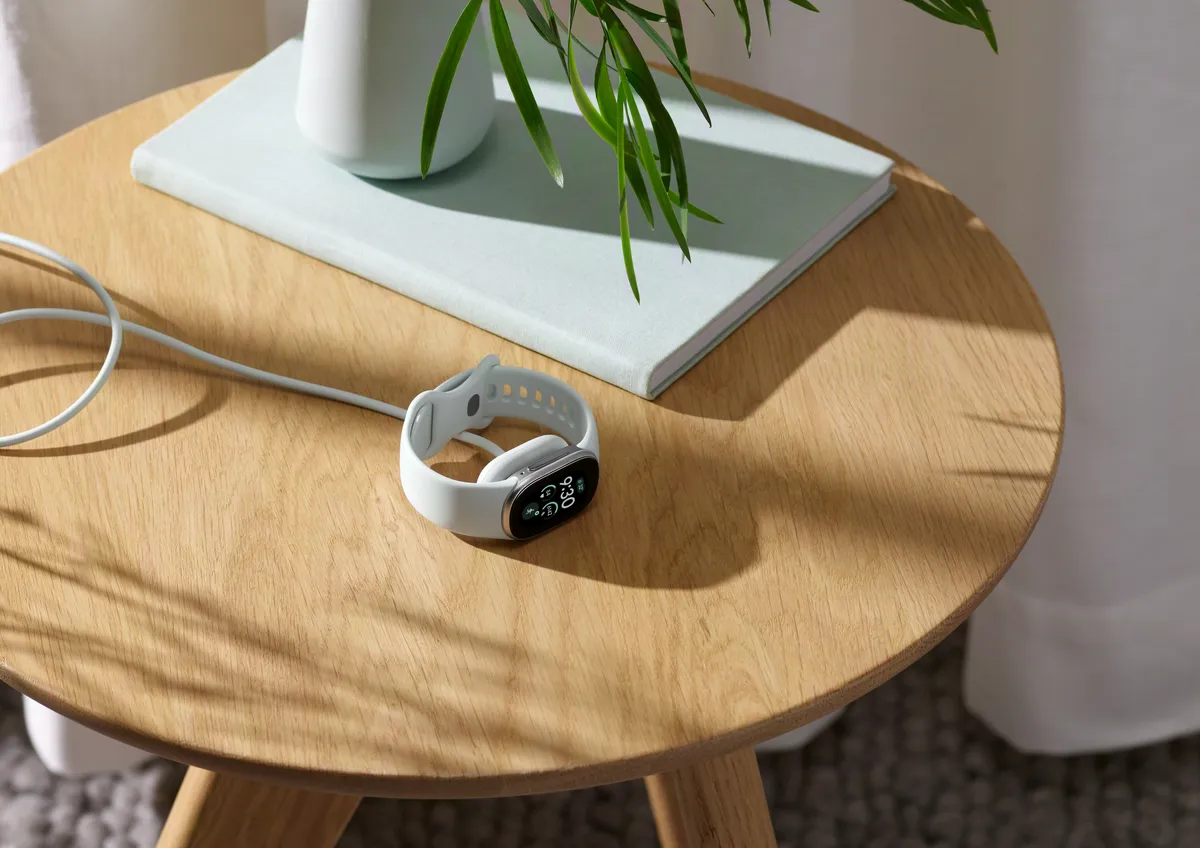 Um Fitbit Edge com pulseira branca carregando em uma mesinha de madeira